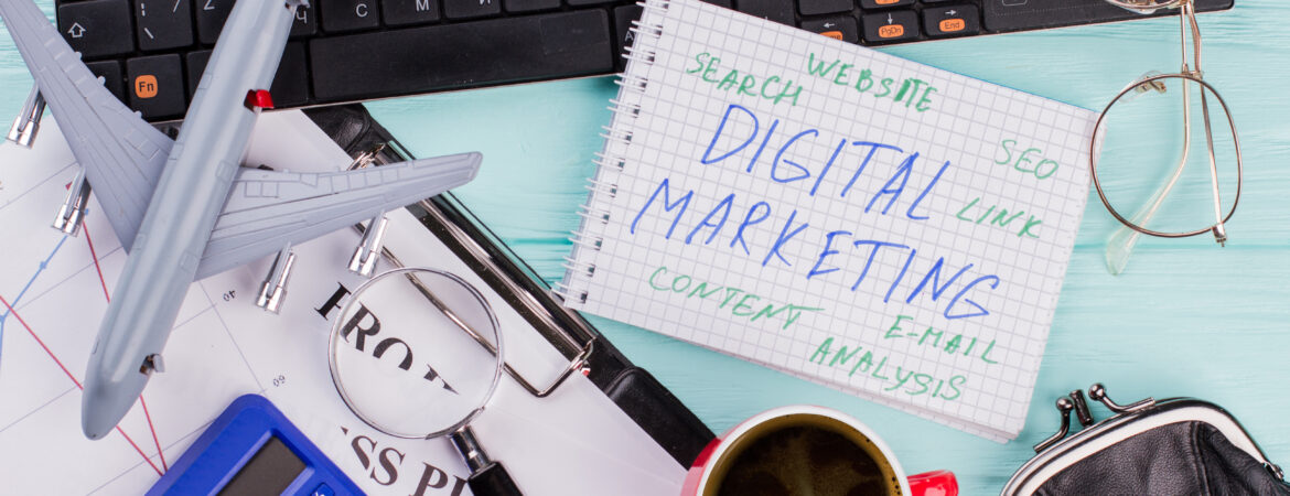 Digital marketing on notepad and various office supplies. Flat lay composition with keyboard, coffee and other office related objects on blue background.