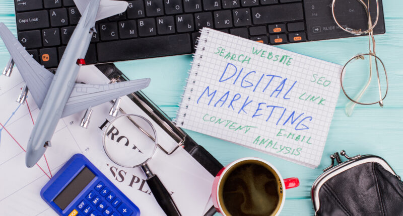 Digital marketing on notepad and various office supplies. Flat lay composition with keyboard, coffee and other office related objects on blue background.